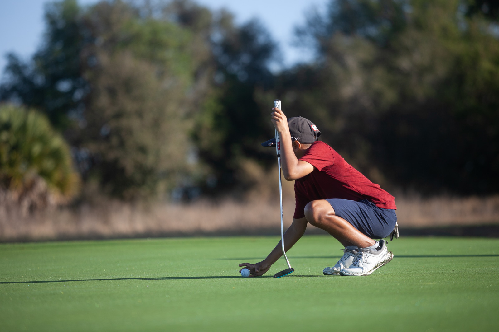 A junior golfer crouching to place a ball on the putting green