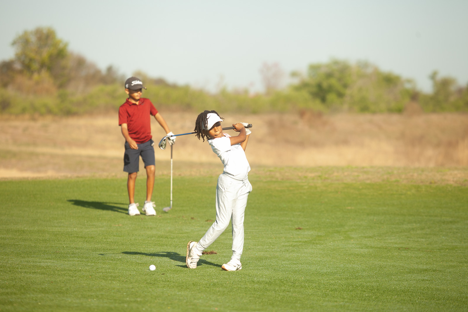 A young golfer completing a swing while another junior golfer watches