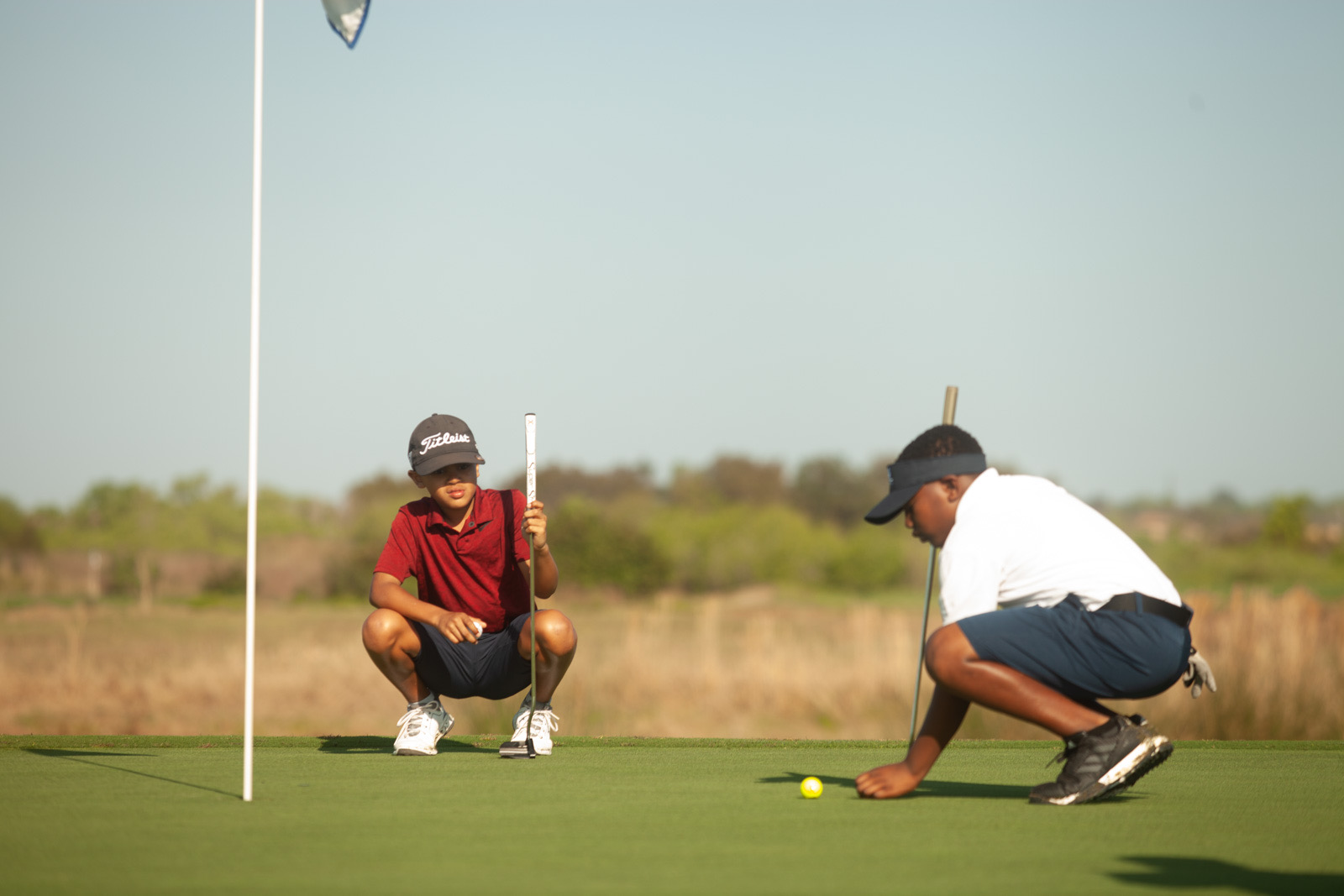 Two junior golfers reading their putts together on the green